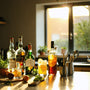 Sunlit kitchen counter set for homemade cocktail fun with fresh herbs, citrus, and a playful mix of spirits