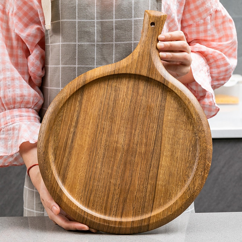 Round wooden chopping board held by a person in a kitchen.