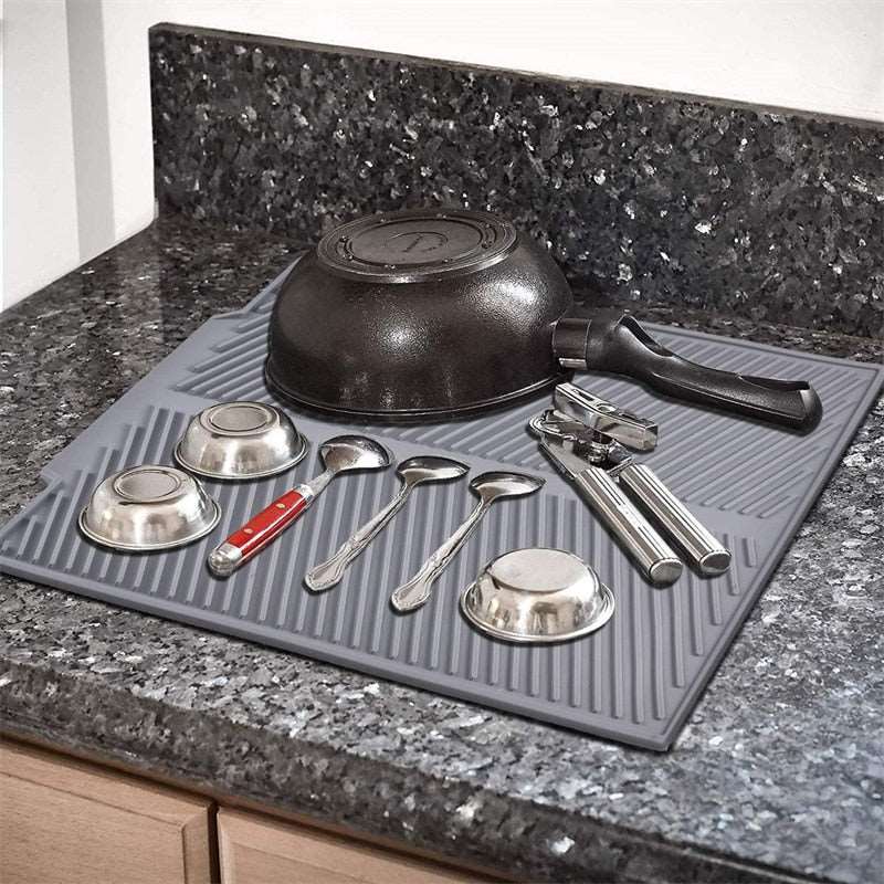 Foldable insulated soft rubber sink mat used as a dish drying pad on a granite countertop with kitchen utensils.