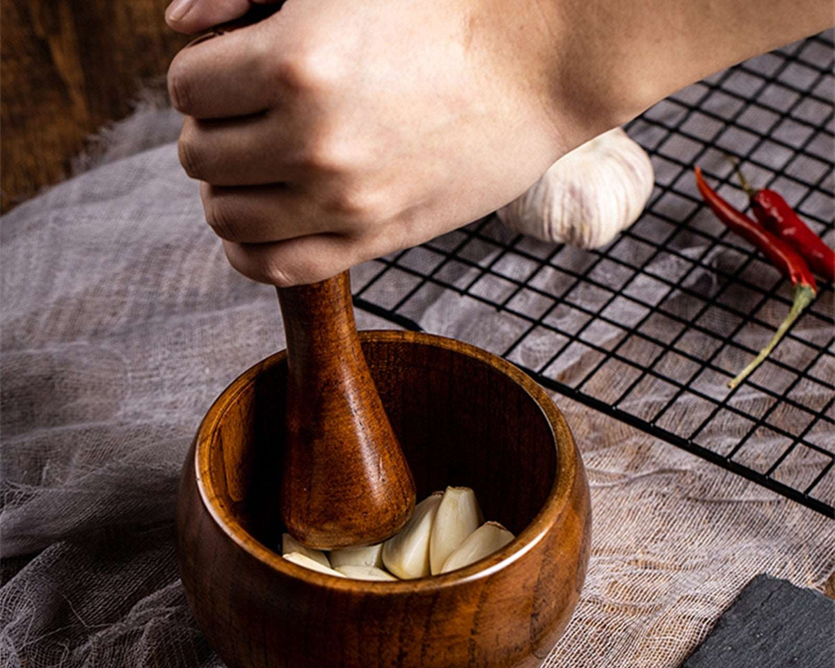 Bamboo wooden mortar and pestle set grinding garlic cloves on a table.
