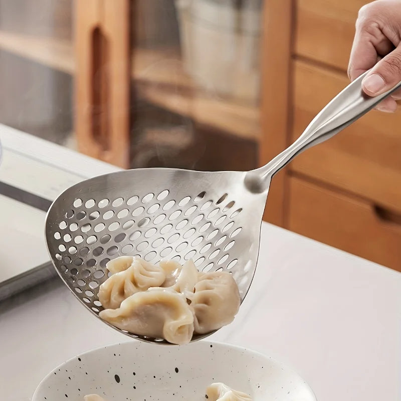 Metallic skimmer with dumplings being lifted from a pot on a kitchen counter.