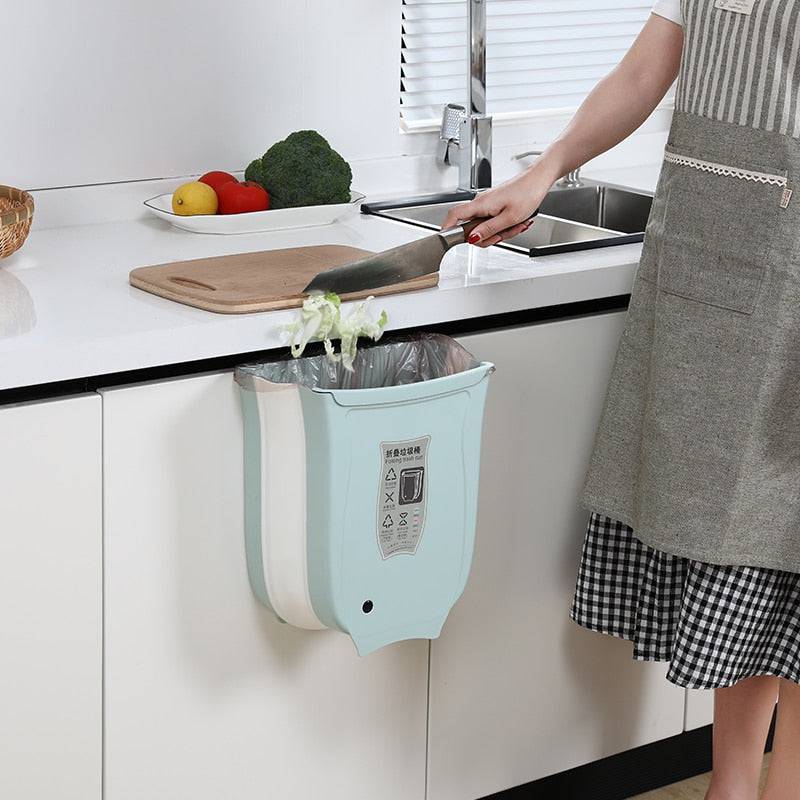 Wall-mounted foldable waste bin on kitchen cabinet, ideal for small spaces and easy trash disposal.