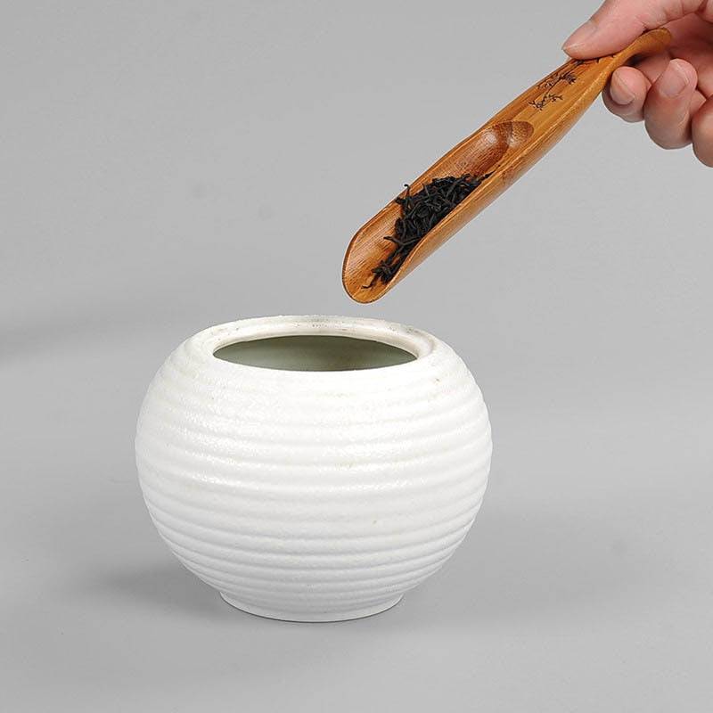 Bamboo fish shape tea shovel in use scooping tea into a white ceramic container.
