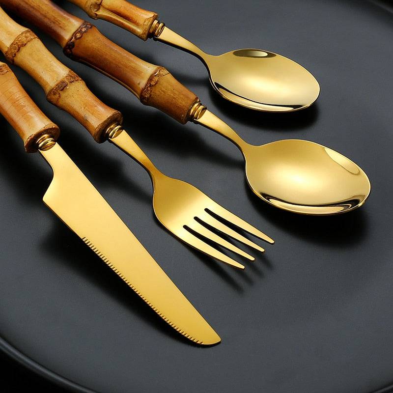 Bamboo handle stainless steel flatware set with gold finish, includes knife, fork, and spoon on a black plate.