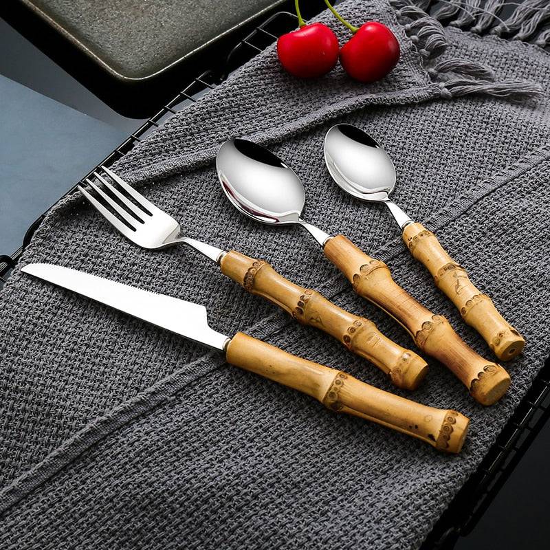 32-piece stainless steel and bamboo handle cutlery set on gray cloth with cherries, includes knife, fork, spoon.