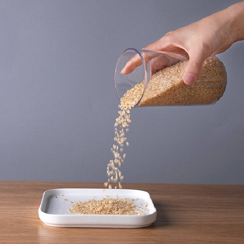 Hand pouring rice from a sealed ring bottle kitchen storage box, transparent food canister.