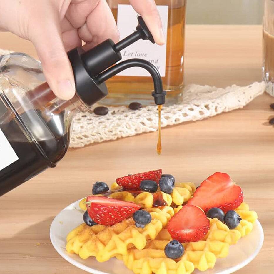 TheWellBeing™ 500ml glass coffee syrup dispenser with steel pump in use over waffles with fruit.