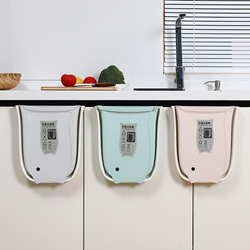 Wall mounted foldable waste bins hanging on kitchen cabinet doors in three colors.
