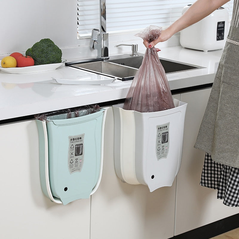 Wall mounted foldable waste bin hanging on cabinet door in kitchen.