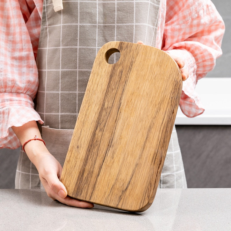 Wooden chopping board held by person in apron on kitchen counter.