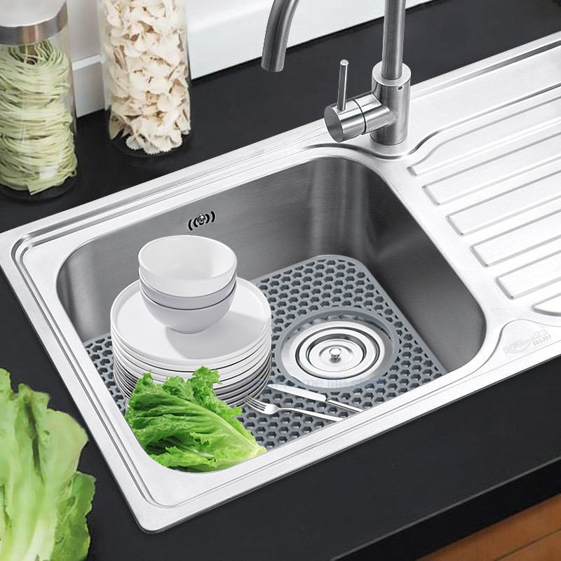 Silicone sink protector mat for stainless steel kitchen sink with bowls and vegetables.
