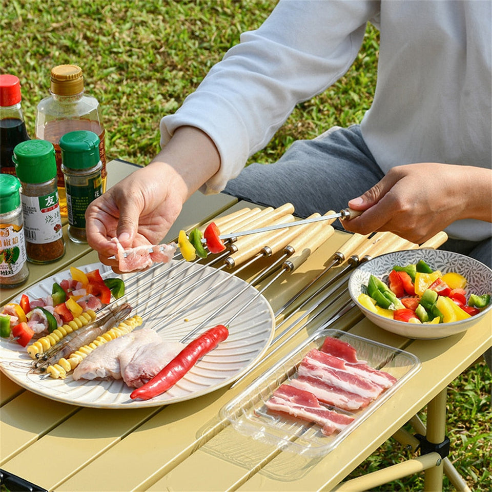 Outdoor BBQ setup with stainless steel reusable skewers for grilling meat and vegetables.